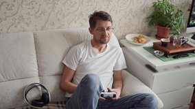 a young man plays a console sitting on the couch. holding joystick in hand