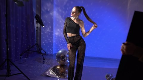 Girl in the studio at a photo shoot with neon lights and disco-ball. Front view