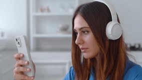 Charming girl surfing news on smartphone and enjoying favorite songs in wireless headphones