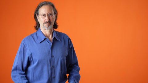 Promoter mature long hair bearded man 50s 60s orange shirt point fingers aside on workspace copy space mockup promo commercial area isolated on solid orange background studio portrait