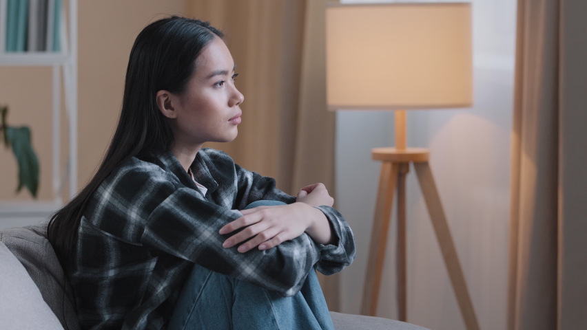 Side view sad asian woman sitting on couch at home feeling unsure about hard decision unhappy bad feeling mental trouble sits on sofa. Depressed korean lady regretting mistake psychological trouble | Shutterstock HD Video #1089151167