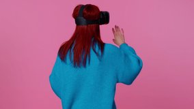 Amazed teen student girl using headset helmet app to play simulation game. Watching virtual reality 3D 360 video. Young woman in VR goggles isolated on pink background. Addiction from technology