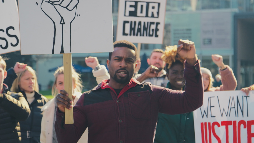 Group of protestors holding placards and chanting slogans on demonstration march to promote black lives matter anti racist beliefs - shot in slow motion