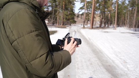 guy photographer takes pictures on camera in the forest. shoot winter forest landscapes. male photographer with beard