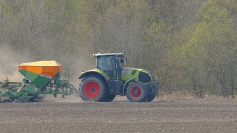 Tallinn Estonia 2021 April 02: A green tractor with the bin on the back in Tallinn Estonia plowing the soil of the emtpy field