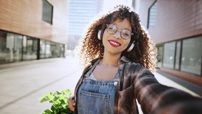 Outdoors POV portrait of cheerful mixed race woman with curly hair chatting and waving hand making video call outside in city during sunset, lifestyle video.