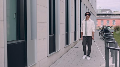 Young asian blind man with using safety stick for walking alone outdoors. Male person wearing glasses and casual clothes. Independence concept
