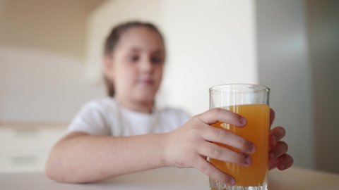girl child drinking juice. happy family a healthy eating kid dream concept. daughter girl drinking yellow juice from a glass cup in the kitchen. child drinking indoors fruit juice