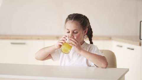 girl child drinking juice. happy family a healthy eating kid dream concept. daughter girl indoors drinking yellow juice from a glass cup in the kitchen. child drinking fruit juice