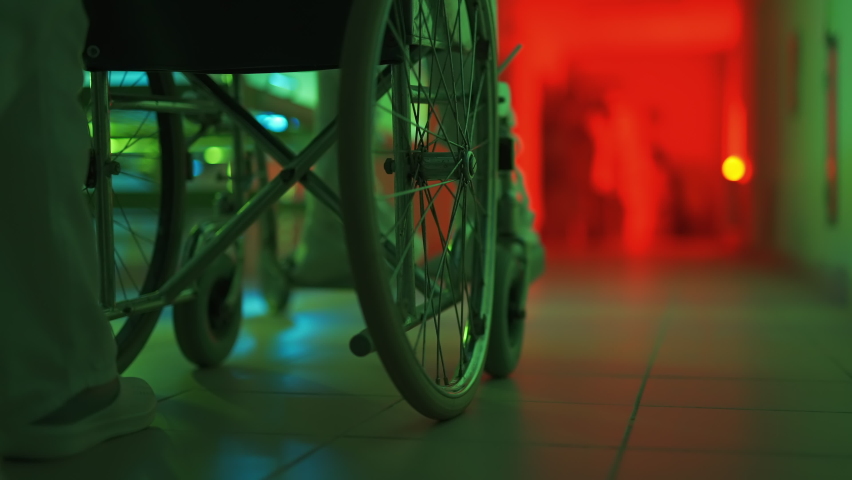 A paramedic is driving a mad male patient in wheelchair down corridor in mental hospital. Ill person in straitjacket is going crazy. Concept of paranoia or schizophrenia and madness. Wheels close up. Royalty-Free Stock Footage #1089158839
