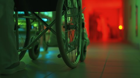 A paramedic is driving a mad male patient in wheelchair down corridor in mental hospital. Ill person in straitjacket is going crazy. Concept of paranoia or schizophrenia and madness. Wheels close up.