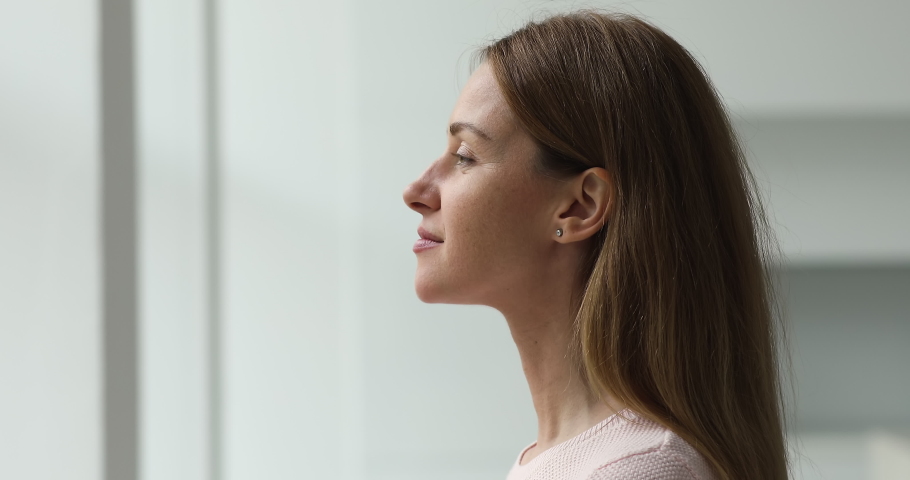 Calm young woman taking deep breath of fresh air meditating with eyes closed standing indoor, close up side profile view. Enjoy moment of peace, do mental relaxation exercises, feels no stress concept | Shutterstock HD Video #1089159033