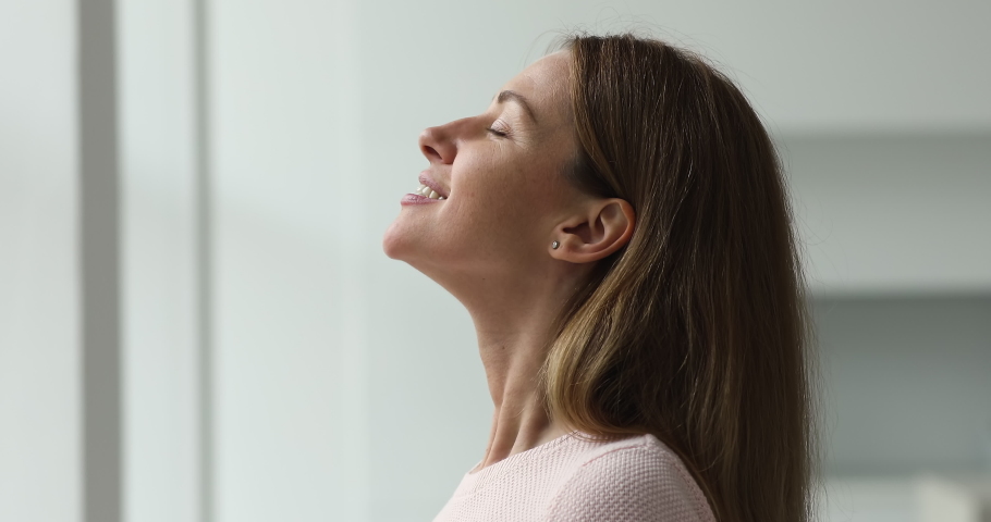Calm young woman taking deep breath of fresh air meditating with eyes closed standing indoor, close up side profile view. Enjoy moment of peace, do mental relaxation exercises, feels no stress concept | Shutterstock HD Video #1089159033
