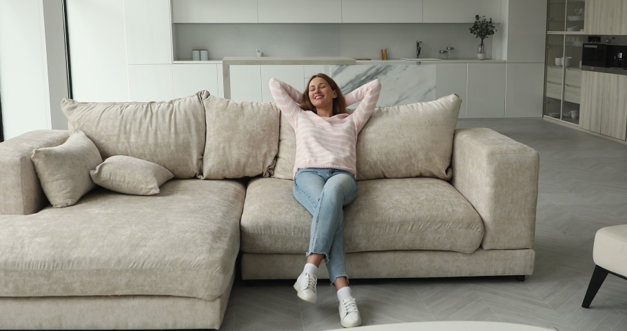 Full-length view, relaxed woman put hands behind head, lean on cozy sofa cushions, rest at home daydreams, enjoy stress-free weekend in fashionable living room. Leisure, climate control inside concept Royalty-Free Stock Footage #1089159095