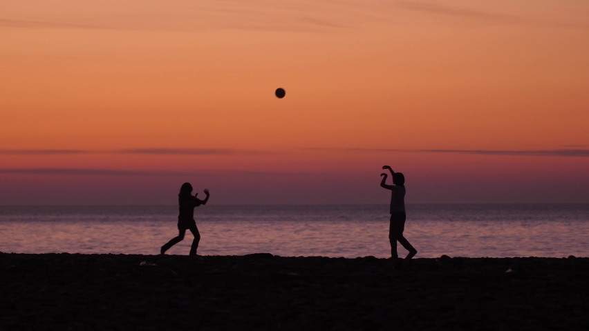 Two kids are playing volleyball in the sunset