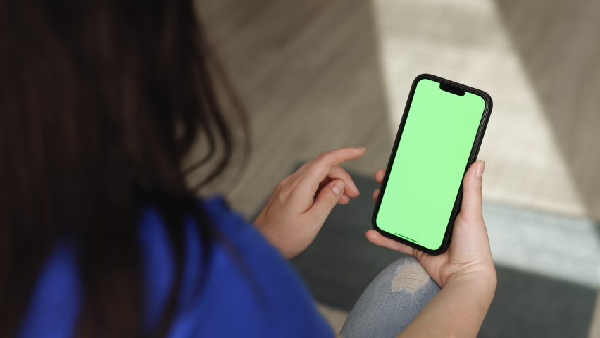 Closeup of woman holds mobile phone smartphone and swipes photos or pictures left indoors of cozy home. Chroma key mock-up on smartphone in hand. Use green screen for copy space. Royalty-Free Stock Footage #1089165551