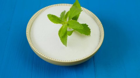 Stevia twig in a green round bowl with white stevia powder on a blue wooden background.Stevia rebaudiana. View from above.Organic natural sweetener.Stevia plants. 4k footage