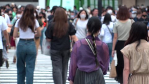 TOKYO, JAPAN - AUG 2020 : Back shot and crowd of people wearing surgical mask to protect from Coronavirus (COVID-19) at Shibuya Crossing. Slow motion shot in summer day time. Japanese medical concept.