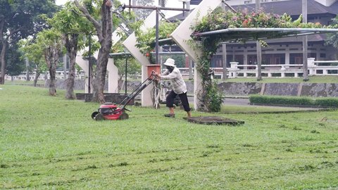Jakarta, Indonesia - April 12, 2022: Asian man mowing lawn in the garden.  Mowing or cutting the long grass with electric lawn mower
