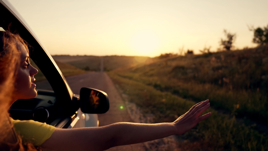 Happy girl in car window. Hair in wind. Girl travels by car. Hand in sun. Windy breeze from car window. Happy girl smiling from car window. Windy breeze in your hair. Hand in the rays of the sun | Shutterstock HD Video #1089178763