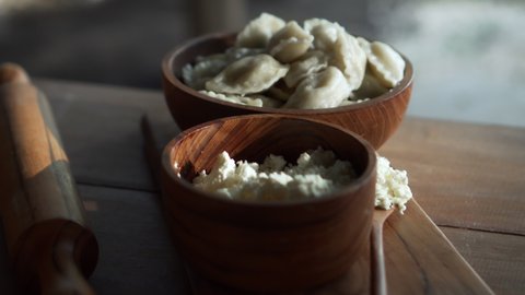 Traditional Russian fresh handmade dumplings lying on a wooden table on a cutting board with cottage cheese in a wooden plate