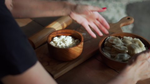 Traditional Russian fresh handmade dumplings lying on a wooden table on a cutting board with cottage cheese in a wooden plate