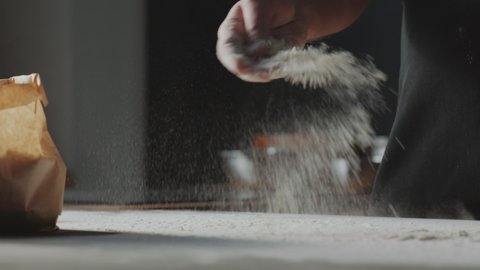 Tracking close up shot of male chef talking flour from paper bag and sprinkling it on table