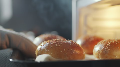 Close up shot of hand in oven glove taking baking sheet with hot burger buns from oven: stockvideo