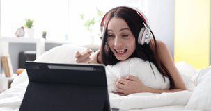 Cheerful happy woman in headphones sings song and lies on bed