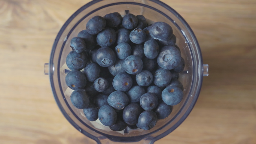 Running blender mixing raw blueberries and fresh milk, making a healthy delicious shake, top down view. Royalty-Free Stock Footage #1089184429