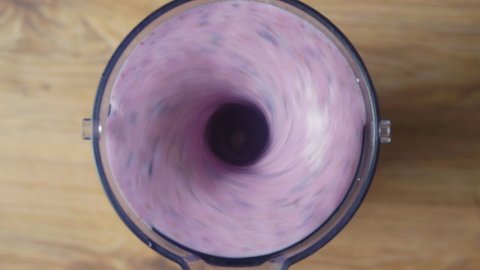 Running blender mixing raw blueberries and fresh milk, making a healthy delicious shake, top down view.