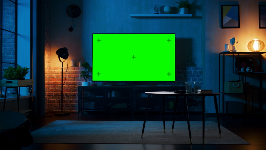 Stylish Loft Apartment Interior with TV Set with Green Screen Mock Up Display Standing on Television Stand. Empty Living Room at Home with Chroma Key Placeholder on Monitor. Panning Right Slider Shot.