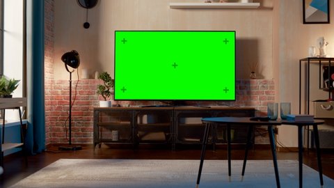 Stylish Loft Apartment Interior with TV Set with Green Screen Mock Up Display Standing on Television Stand. Empty Living Room at Home with Chroma Key Placeholder on Monitor. Zoom Out Shot.