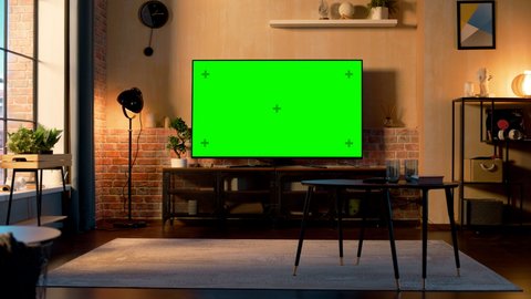 Stylish Loft Apartment Interior with TV Set with Green Screen Mock Up Display Standing on Television Stand. Empty Living Room at Home with Chroma Key Placeholder on Monitor. Panning Right Slider Shot.