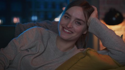 Portrait of Beautiful Female Spending Time at Home, Resting on a Couch, Watching Comedy TV Show in Stylish Loft Apartment. Young Happy Woman Enjoying Movie Streaming Service and Relaxing.