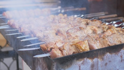 Juicy Pork Kebabs are Fried on an Open Grill in Smoke and Soot. Preparing fried pieces of meat on skewers, on hot coals, baked on the grill. Street fast food trade, sale in the market. Food court.