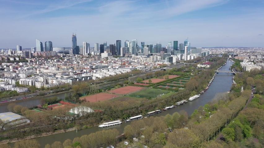 France, Paris, Puteaux island in foreground with moored boat on the Seine river, football field and tennis court, and Modern La Defense parisian business district "French Manhattan". Drone aerial view Royalty-Free Stock Footage #1089190131