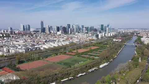 France, Paris, Puteaux island in foreground with moored boat on the Seine river, football field and tennis court, and Modern La Defense parisian business district "French Manhattan". Drone aerial view