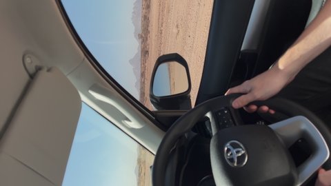 ETOSHA, NAMIBIA - NOVEMBER, 10, 2021: Vertical video. Driving Toyota SUV car. Man driver hands on steering wheel. Steer with logo brand. Country dirt road in Africa. Summer sunny day. Vehicle indoors.