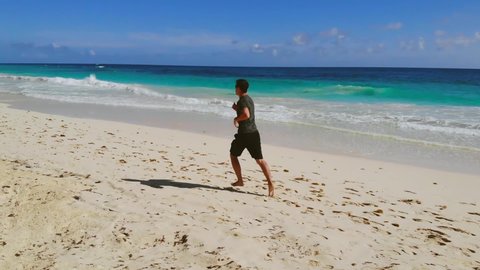 Athletic man jogger running at nature beach sea landscape. Male runner barefoot training at coast scenery practicing intensive cardio activity healthy lifestyle. Back side, slow motion running man.