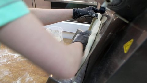 Professional cook is using the special rolling machine for stretching dough at commercial kitchen, close-up 4k footage