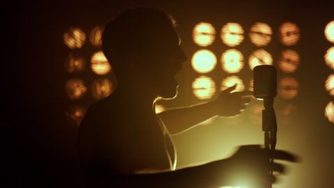 Silhouette unknown performer singing emotional on stage show close up. Professional vocalist performing firely in nightclub lights. Unrecognizable young man dancing near microphone with excitement. 