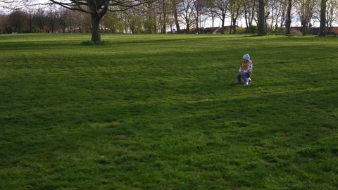 Happy Family Of Children Having Fun In Spring Park. Little Kid Run. Child Girl Sits on Black White Classic Soccer Ball On Green Grass. People Playing Football. Childhood, Sport, Championship Concept