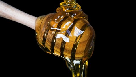 Honey Dripping to a honey dipper on black background.Healthy organic food concept. Wooden honey spoon.Liquid Organic Honey.