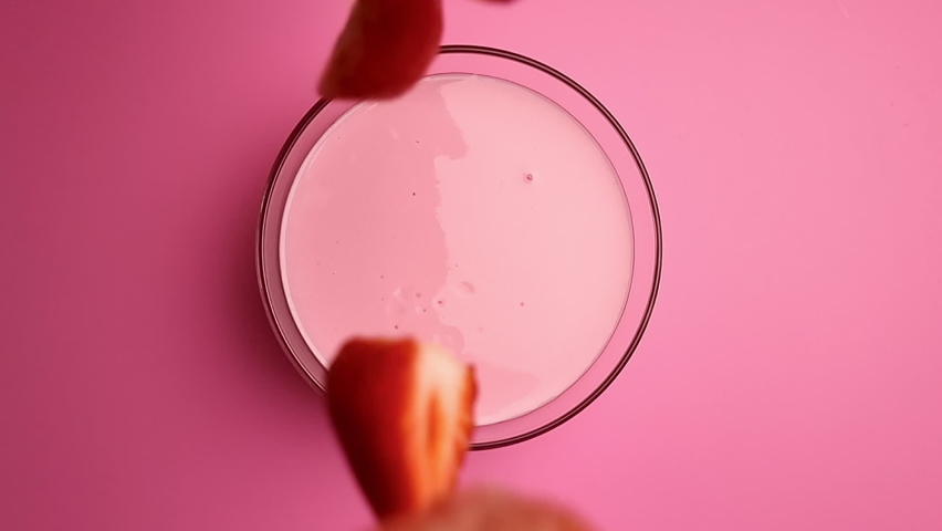 Top view falling fresh seasonal strawberry pieces into creamy yogurt bowl surrounded by splashes slow motion. Appetizing summer dessert dairy milk sweet strawberries delicious berries isolated on pink Royalty-Free Stock Footage #1089199339
