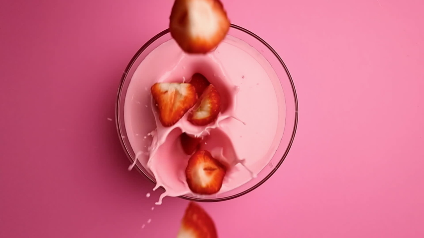 Top view falling fresh seasonal strawberry pieces into creamy yogurt bowl surrounded by splashes slow motion. Appetizing summer dessert dairy milk sweet strawberries delicious berries isolated on pink | Shutterstock HD Video #1089199339