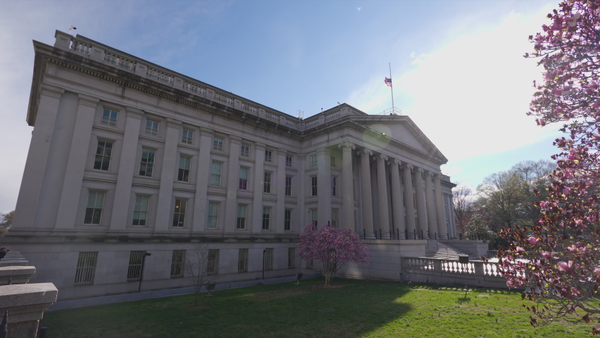 The north entrance of the U.S. Department of the Treasury Building in downtown Washington, D.C. seen on a sunny spring day. A tree with blossoming pink flowers is seen in the foreground. Royalty-Free Stock Footage #1089199511