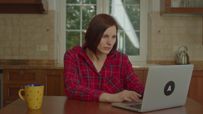 Woman reading bad news on laptop and getting upset and nervous. Sad female using laptop sitting in the kitchen. Royalty-Free Stock Footage #1089200879