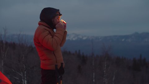 Male tourist leaving camping tent, enjoying view of winter nature and drinking hot tea from steel mug while standing on mountain top Stockvideó