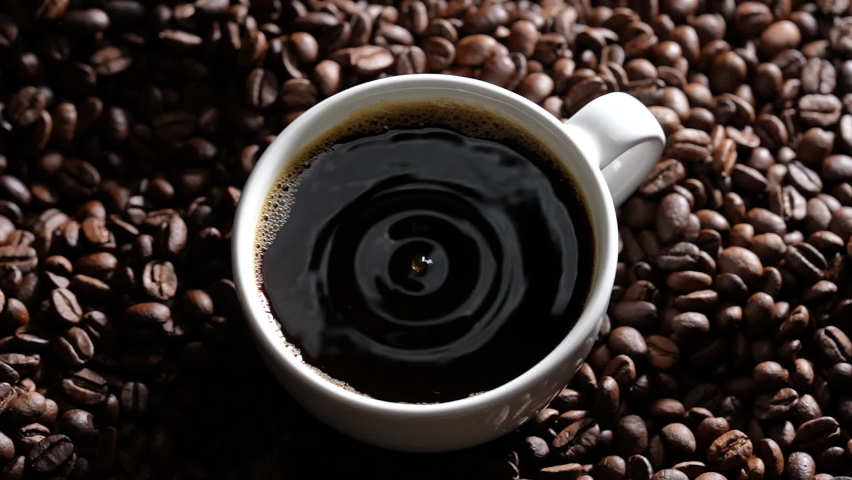 Top view Drop of coffee falling into coffee cup sitting in a pile of freshly roasted coffee beans. Slow motion. | Shutterstock HD Video #1089203797